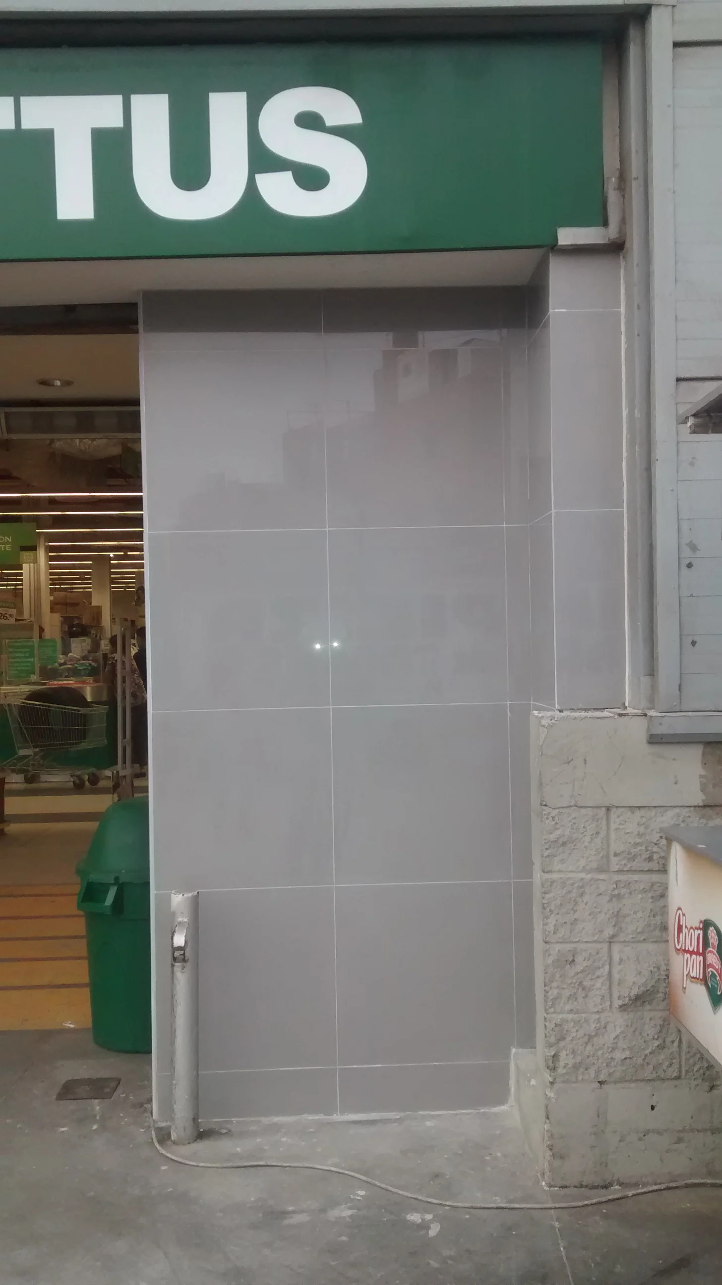 Pared de ingreso a Hipermercado Tottus Quilca con enchape de porcelanato gris de gran formato terminado bajo el tótem verde TOTTUS