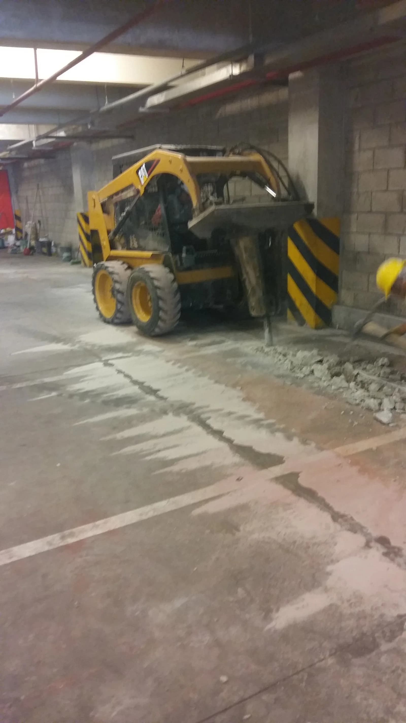 Minicargador CAT amarillo cargando escombros del piso picado en sótano de Tottus La Pólvora durante demolición para trampa de grasa