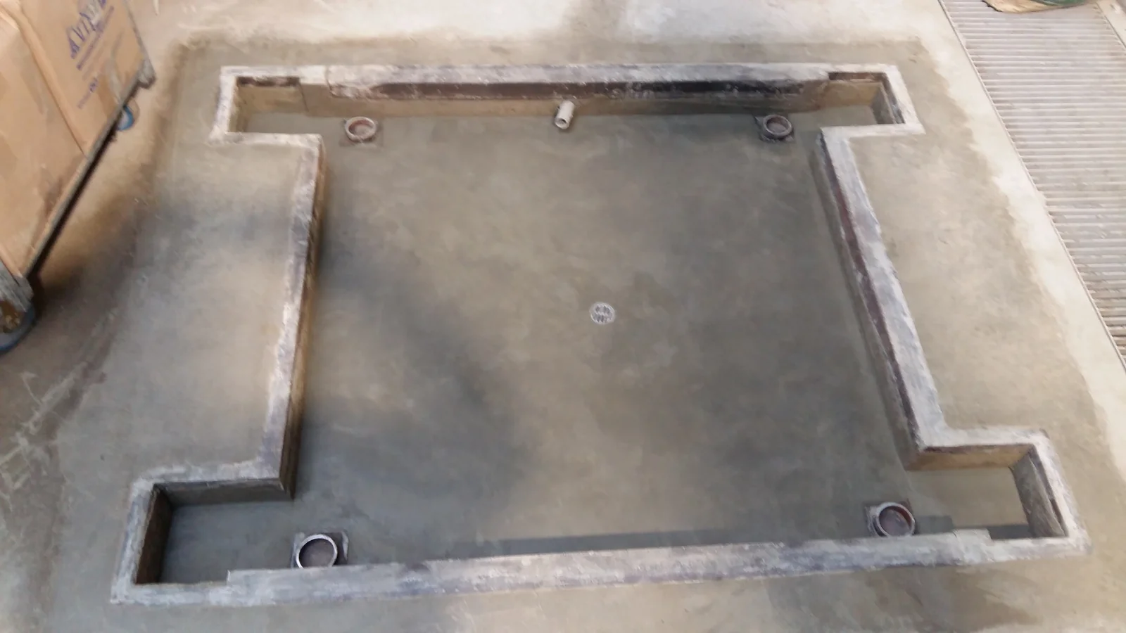 Fosa rectangular de concreto terminada en piso de Tottus Huaycán con bastidor metálico perimetral, cuatro receptáculos para anclajes de balanza electrónica y sumidero central de bronce