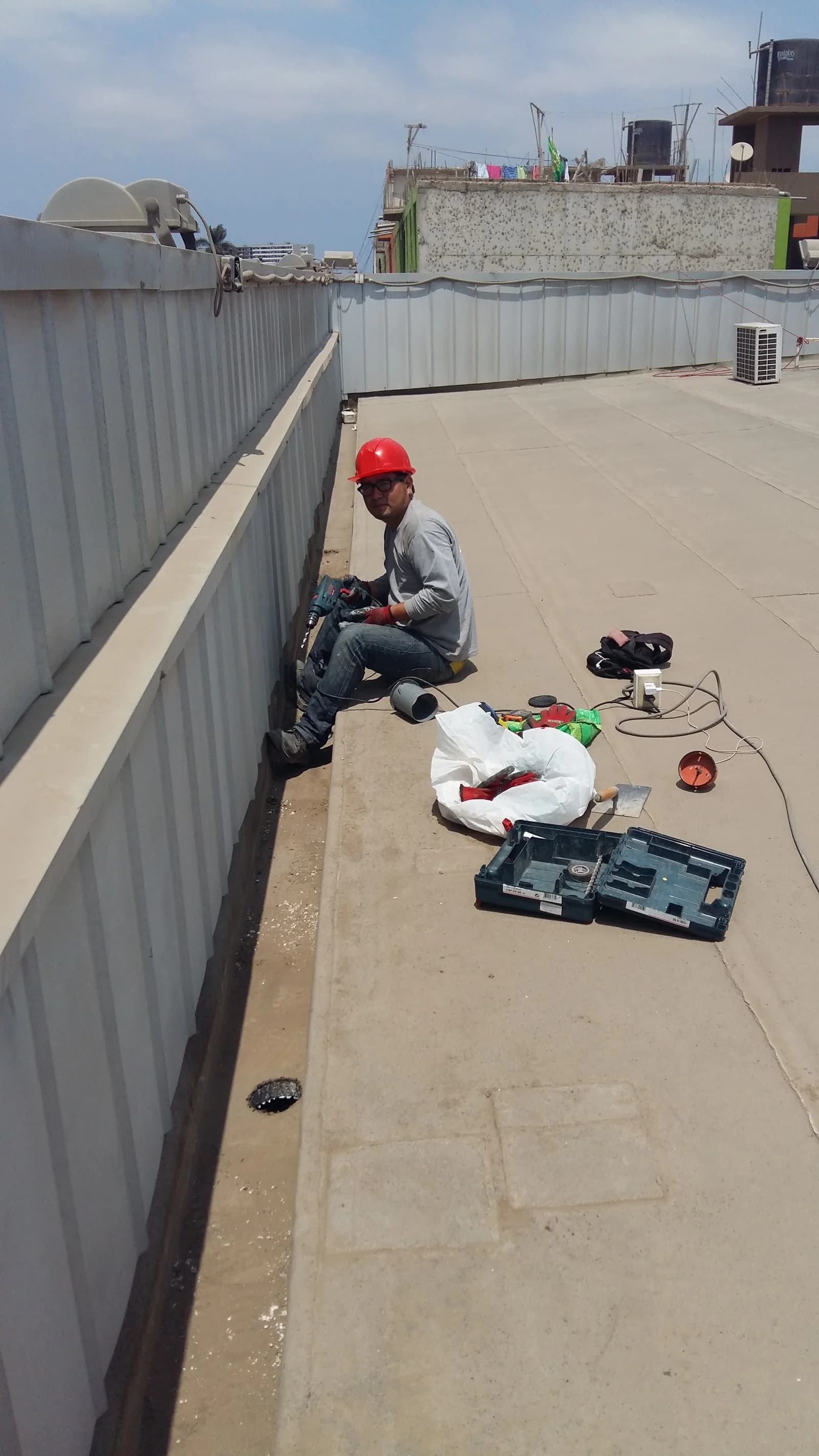 Operario sobre azotea de Tottus Chiclayo perforando el parapeto para instalar sumidero de drenaje pluvial frente a temporada de lluvias
