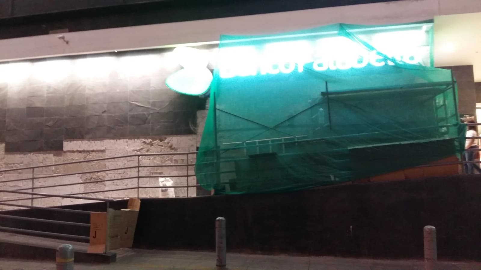 Fachada del Tottus San Luis de noche con andamio cubierto por malla raschel verde sobre el enchape de piedra laja en cambio