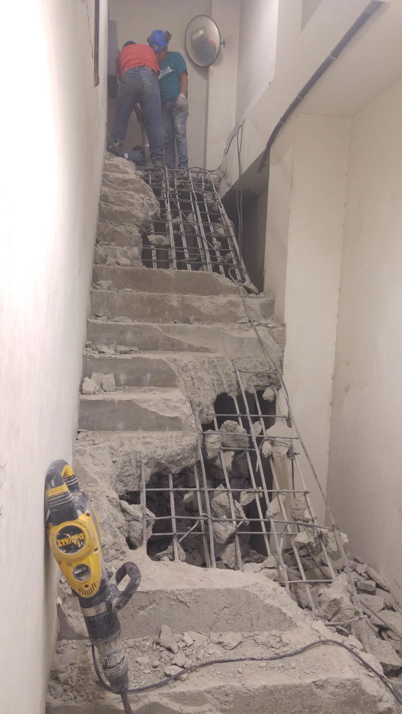 Escalera de concreto armado parcialmente demolida en Tottus Mega Plaza con la malla de acero corrugado expuesta y rotomartillo DeWALT al pie
