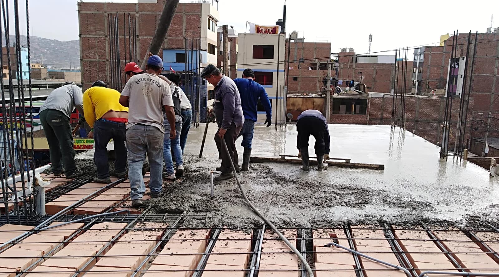Cuadrilla vaciando concreto sobre losa aligerada con ladrillo pastelero en techo de vivienda en San Martín de Porres