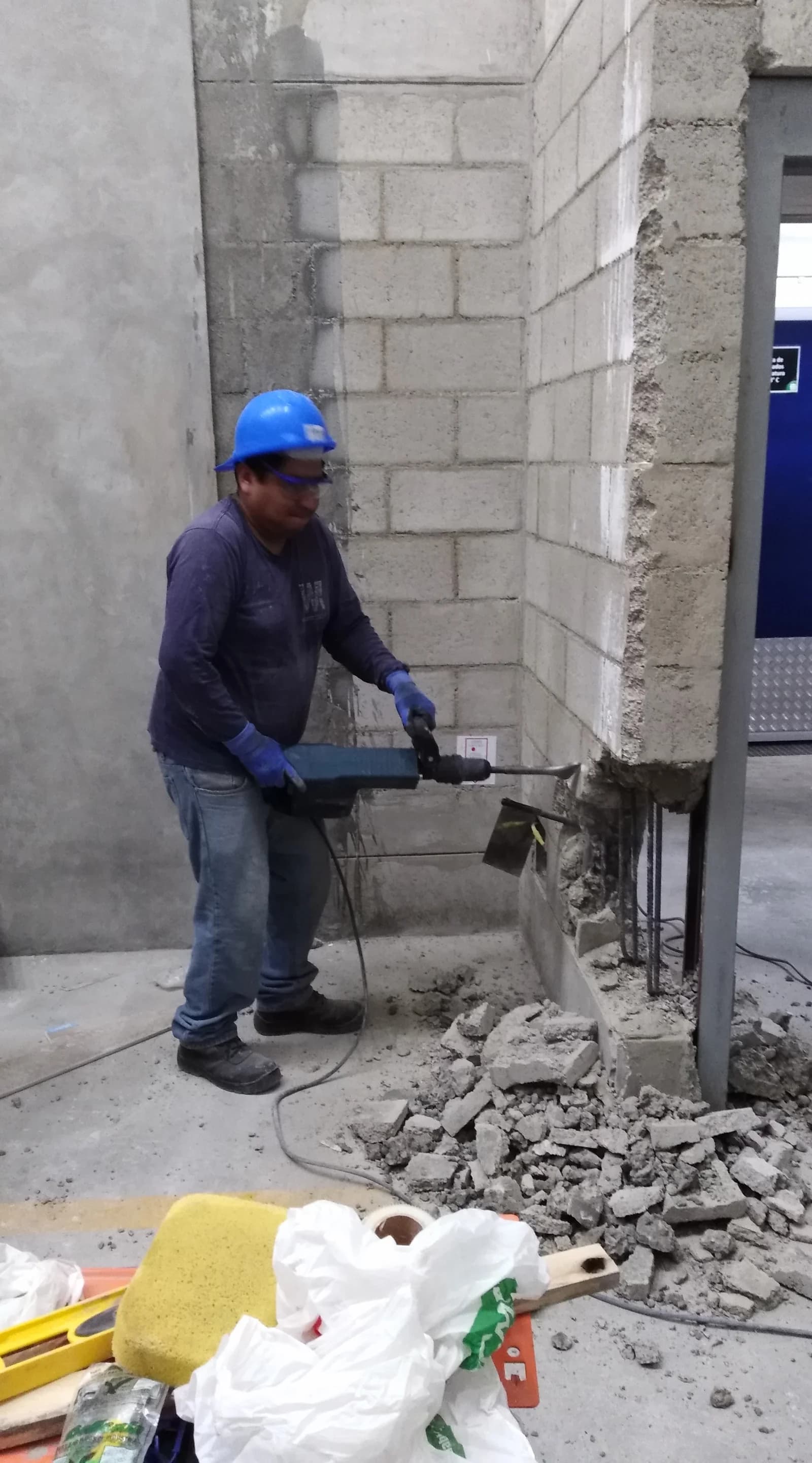 Operario con casco azul demoliendo con rotomartillo eléctrico un muro de bloques de concreto en local Tottus Piura para abrir vano de nueva puerta