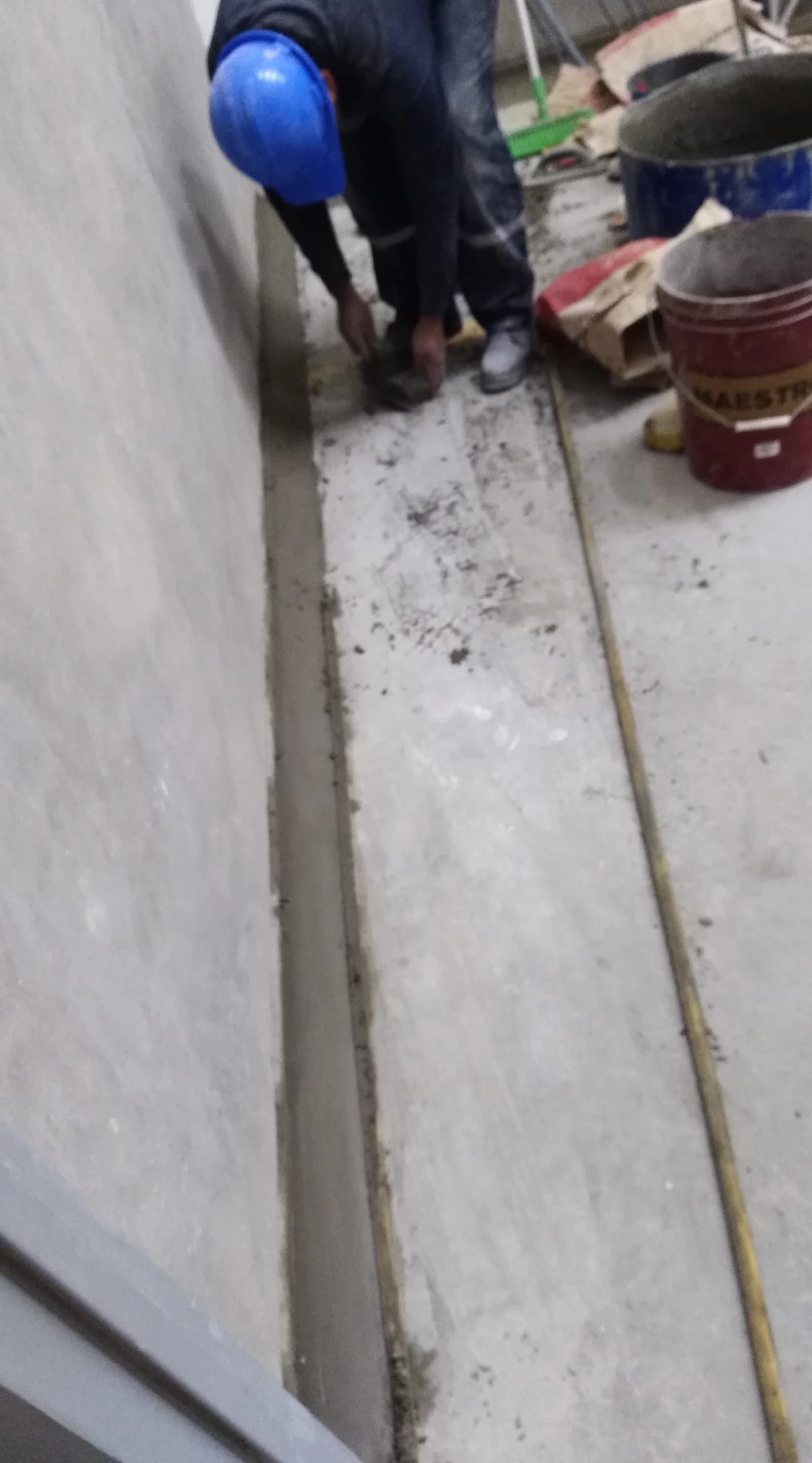 Operario con casco azul modelando con paleta el contrazócalo sanitario curvo en mortero al pie del muro de cámara fría en Tottus Piura