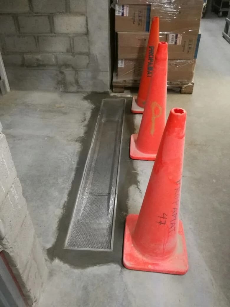Canal de drenaje lineal de acero inoxidable embebido en piso de concreto del almacén de Tottus Piura con paleta de cajas Pamolsa al fondo
