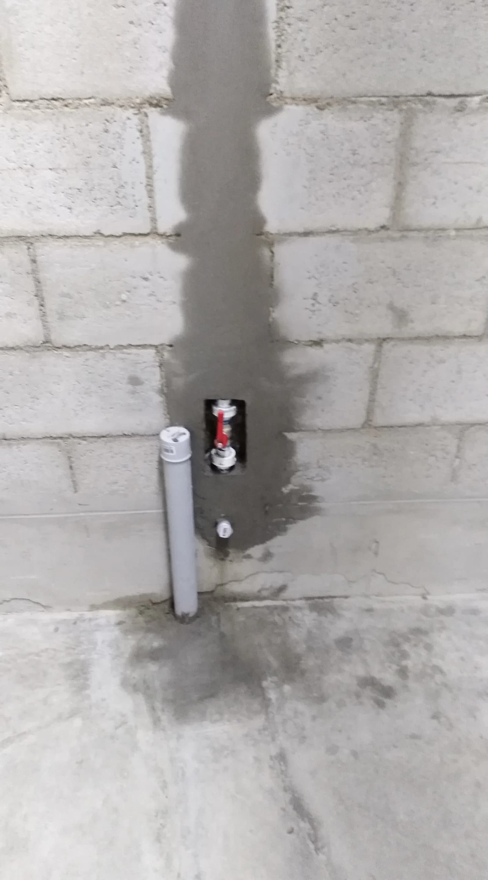 Llave de paso de bola con manija roja instalada y embutida en muro de bloques de concreto con resane de mortero en Tottus Piura