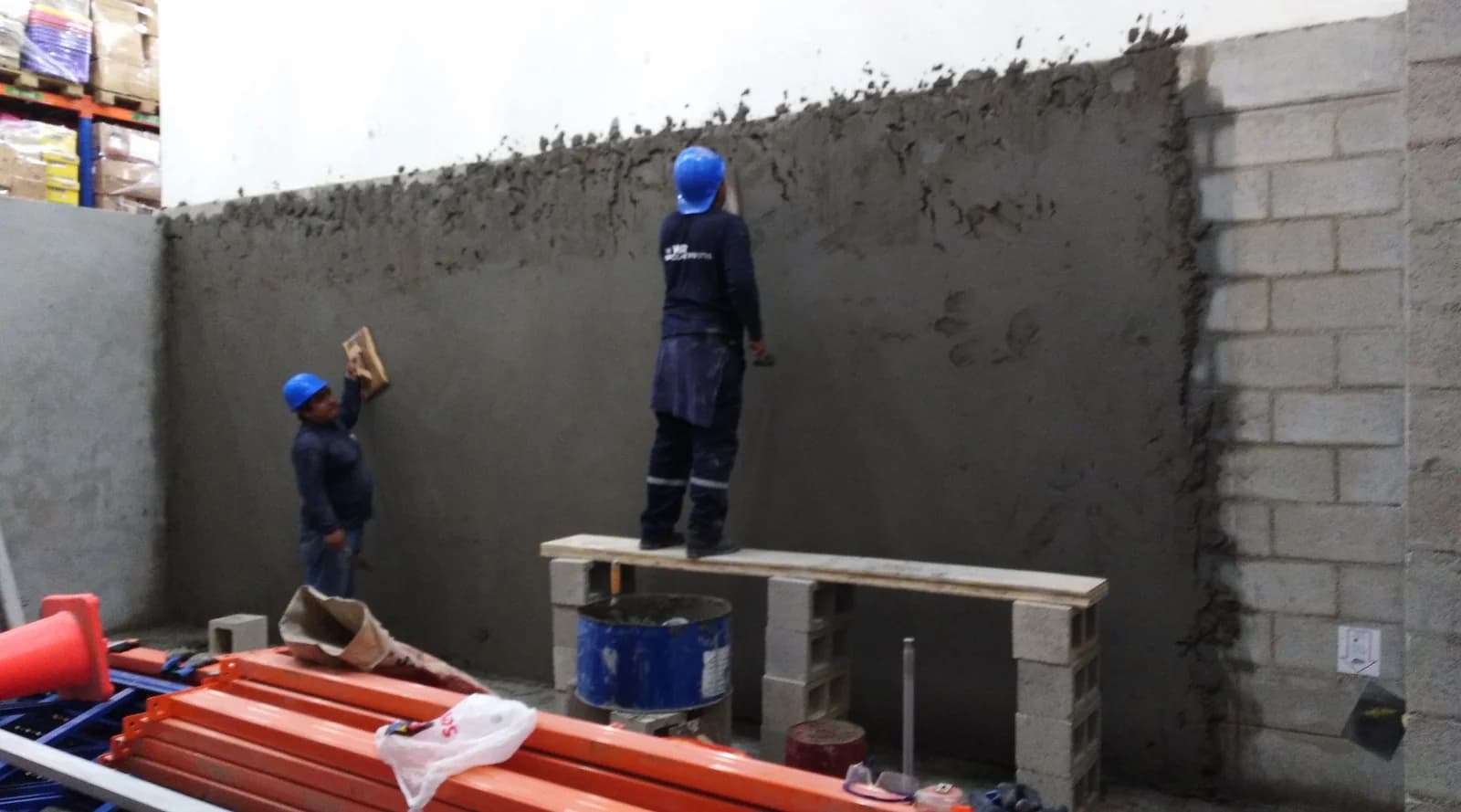 Cuadrilla tarrajeando la pared divisoria de bloques de concreto a doble altura dentro del almacén Tottus Piura