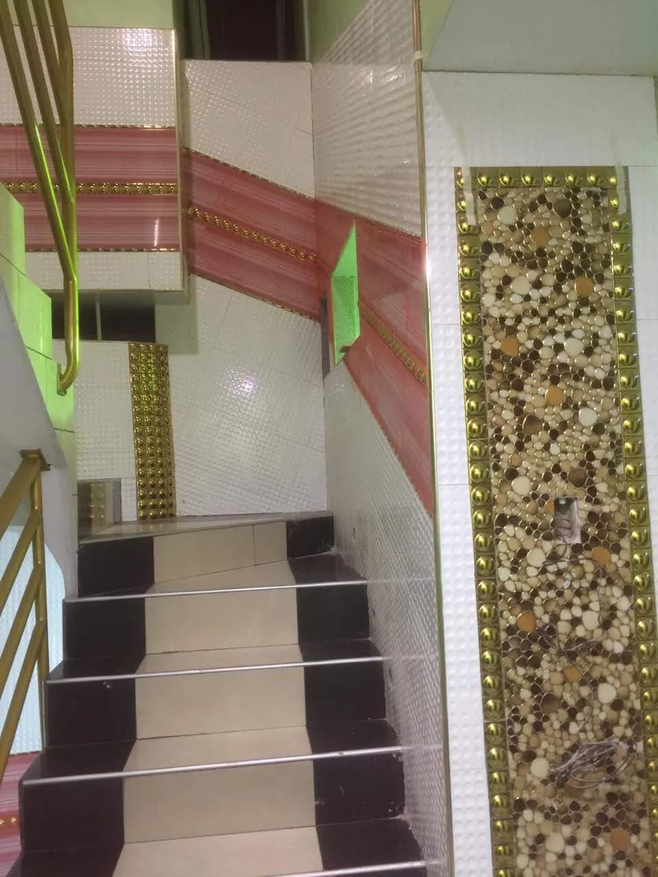 Escalera terminada con peldaños de mármol crema, contrapasos negros y barandal metálico dorado en vivienda de San Miguel